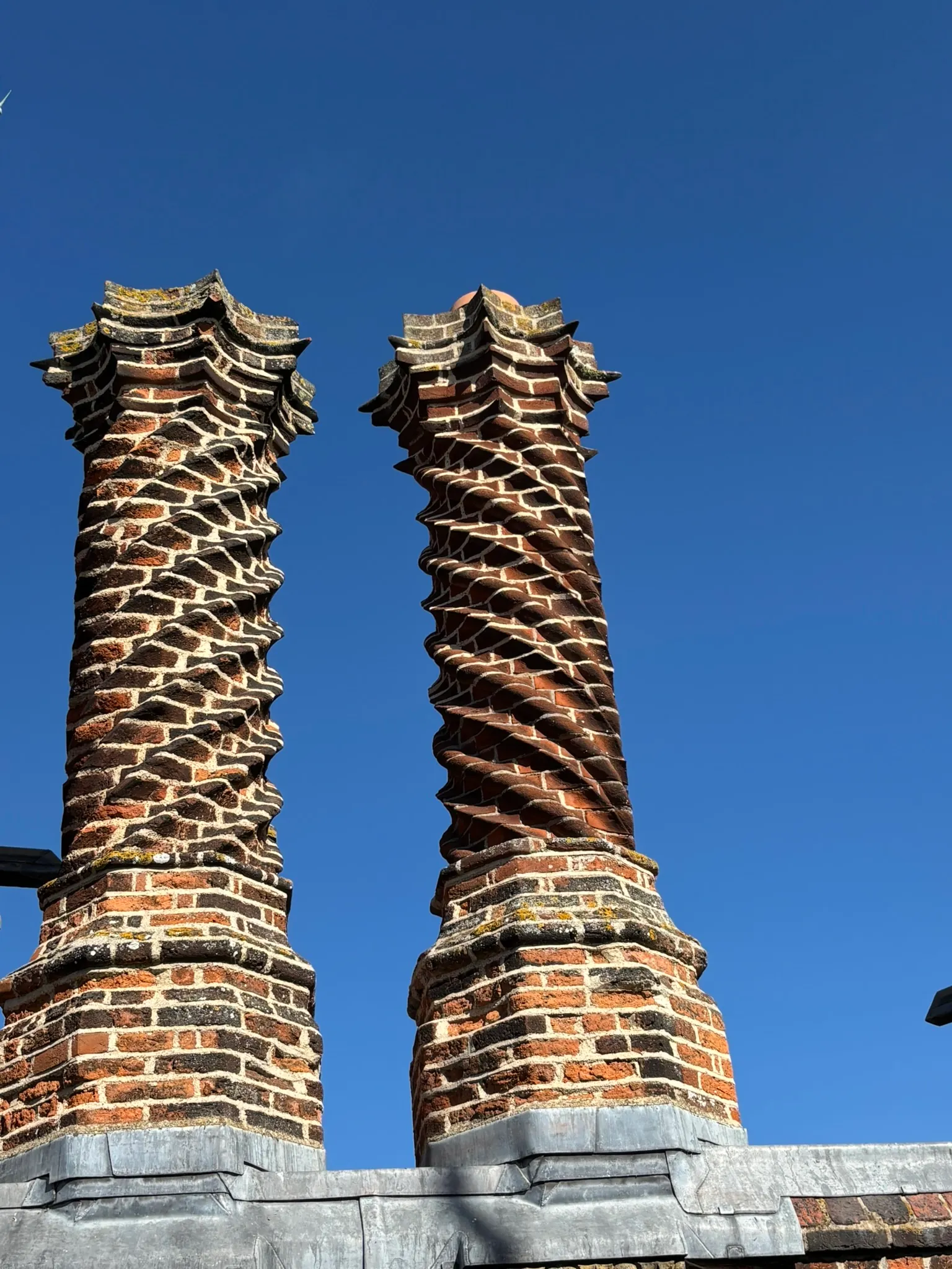 Decorative twisted brick chimneys at Layer Marney Tower against a blue sky.
