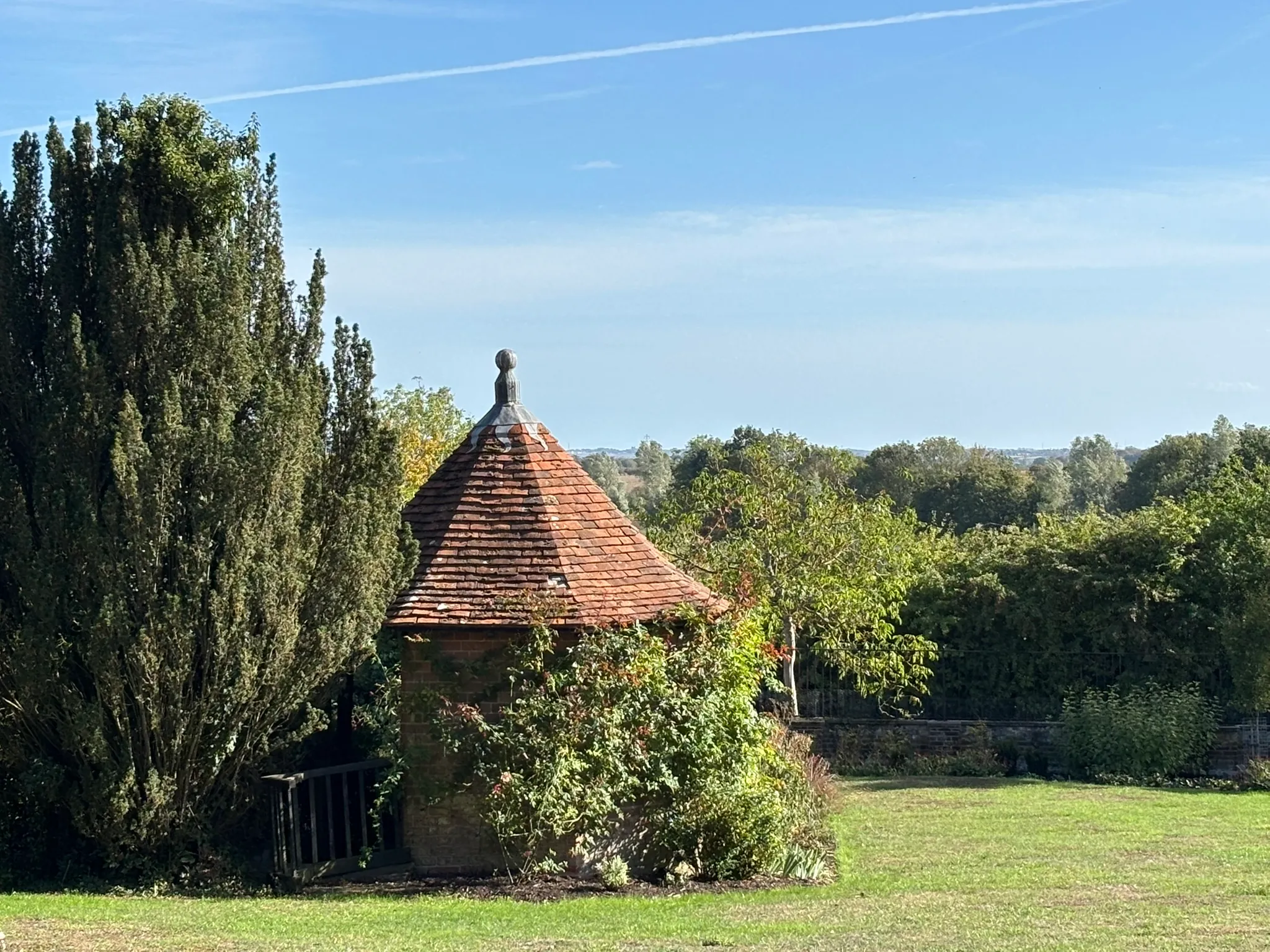 Garden at Layer Marney Tower with a small brick pavilion surrounded by trees and planting.