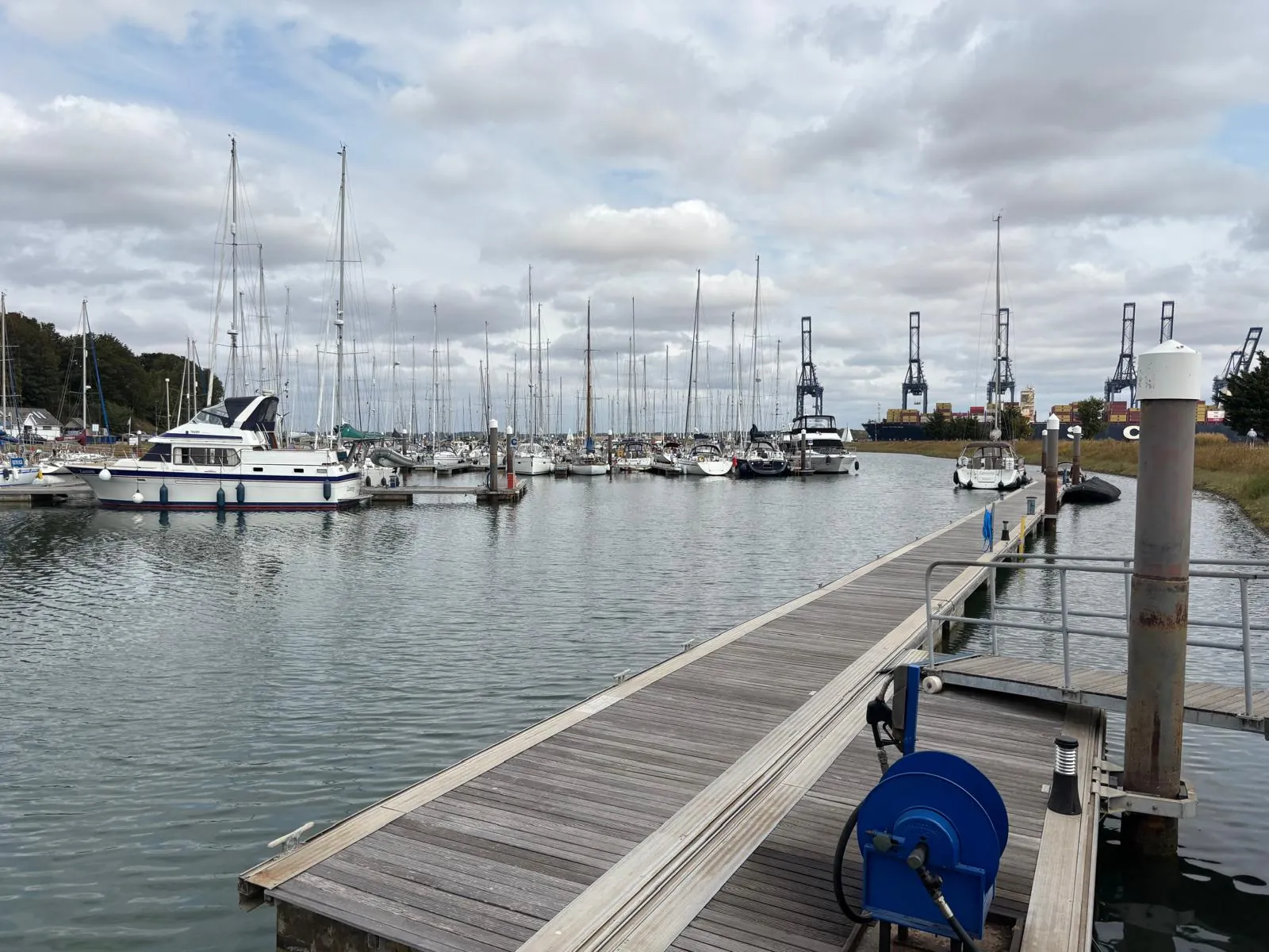 Boats moored in Shotley Marina with container cranes at Felixstowe beyond.